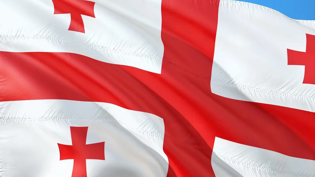 A close-up view of the flag of Georgia, a country in the Caucasus region, with a blue sky in the background.